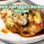 Alice Springs Chicken served on a rustic white plate, topped with sautéed mushrooms, melted cheese, crispy bacon, and chopped green onions.