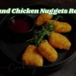 “A plate of crispy chicken nuggets with a golden breadcrumb coating, served with dipping sauce and garnished with fresh vegetables.”