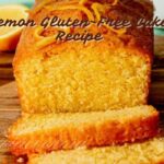 "A moist and fluffy gluten-free lemon cake layered with creamy lemon buttercream frosting, garnished with fresh lemon slices and lemon zest, presented on a white cake stand against a light background."