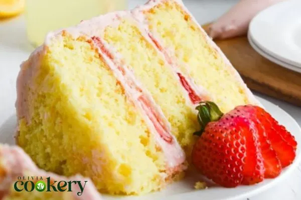 A moist and fluffy strawberry lemon cake topped with lemon frosting and garnished with fresh strawberries and lemon zest.
