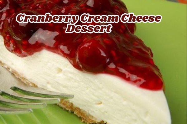 Slice of cranberry cream cheese dessert with a graham cracker crust, creamy cheese layer, and glossy cranberry topping, served on a green plate with a fork and the text "Cranberry Cream Cheese Dessert"